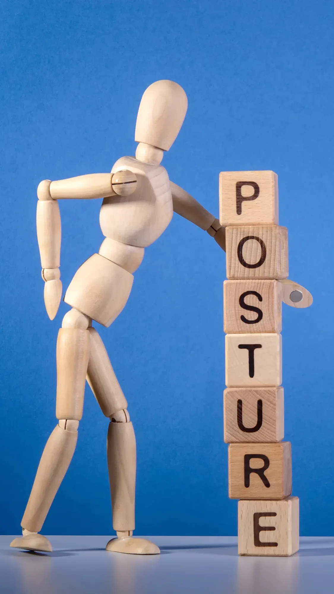 Wooden figure standing next to stacked blocks that spell "Posture"